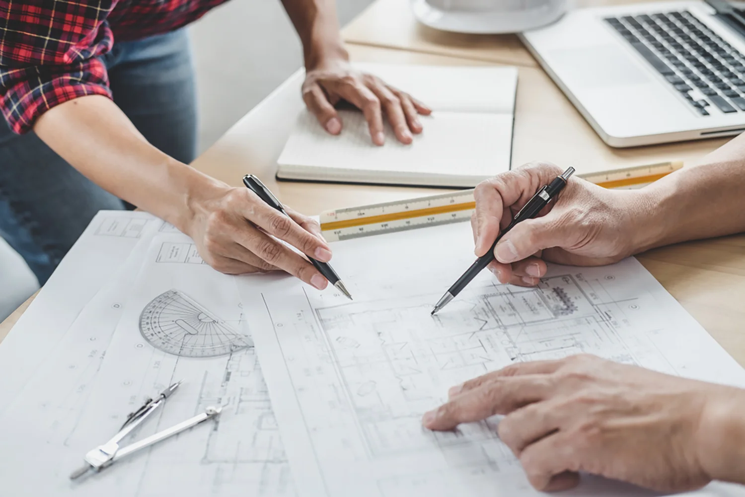 Zwei Personen begutachten architektonische Entwürfe zur Praxisplanung an einem Schreibtisch; eine schreibt Notizen, während die andere auf die Pläne zeigt.