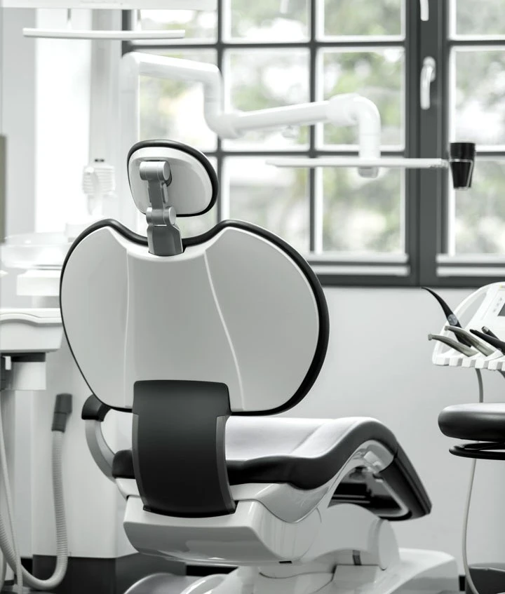 In einer sauberen, hellen Zahnarztpraxis stehen ein moderner Behandlungsstuhl und die Geräte vor einem großen Fenster.