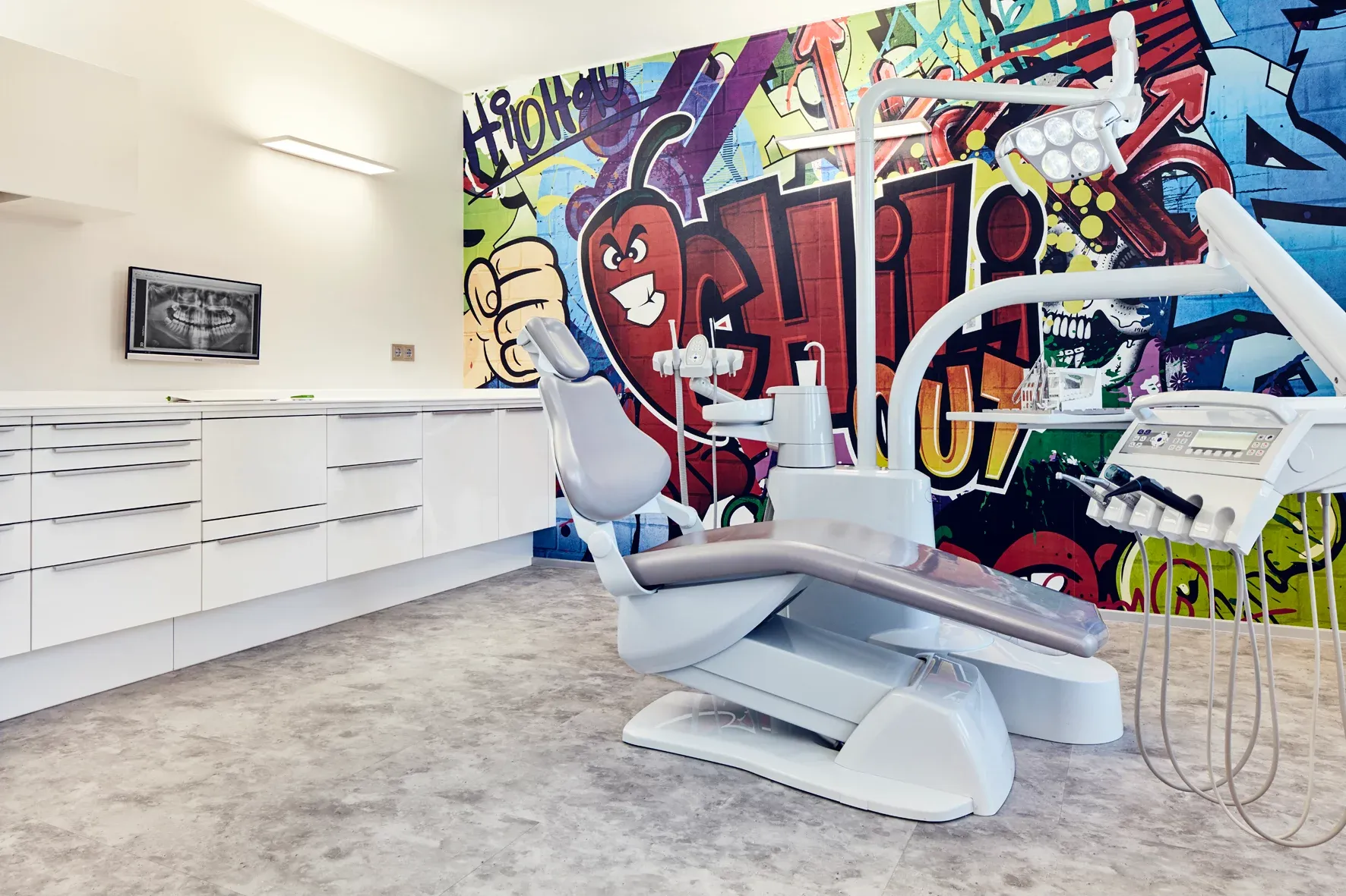 Behandlungszimmer mit moderner Behandlungseinheit und großem Graffiti-Schriftzug „Chili“ an der Wand.