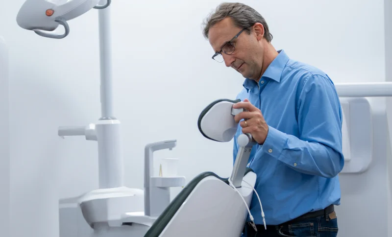 Ein Mann mit Brille und blauem Hemd prüft in einer modernen, hell erleuchteten Zahnklinik die zahnärztliche Ausrüstung.