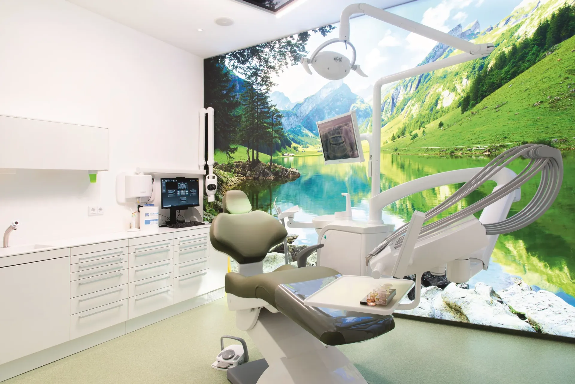 Behandlungszimmer mit moderner Behandlungseinheit und großem Wandbild eines Bergsees zwischen Bergen.