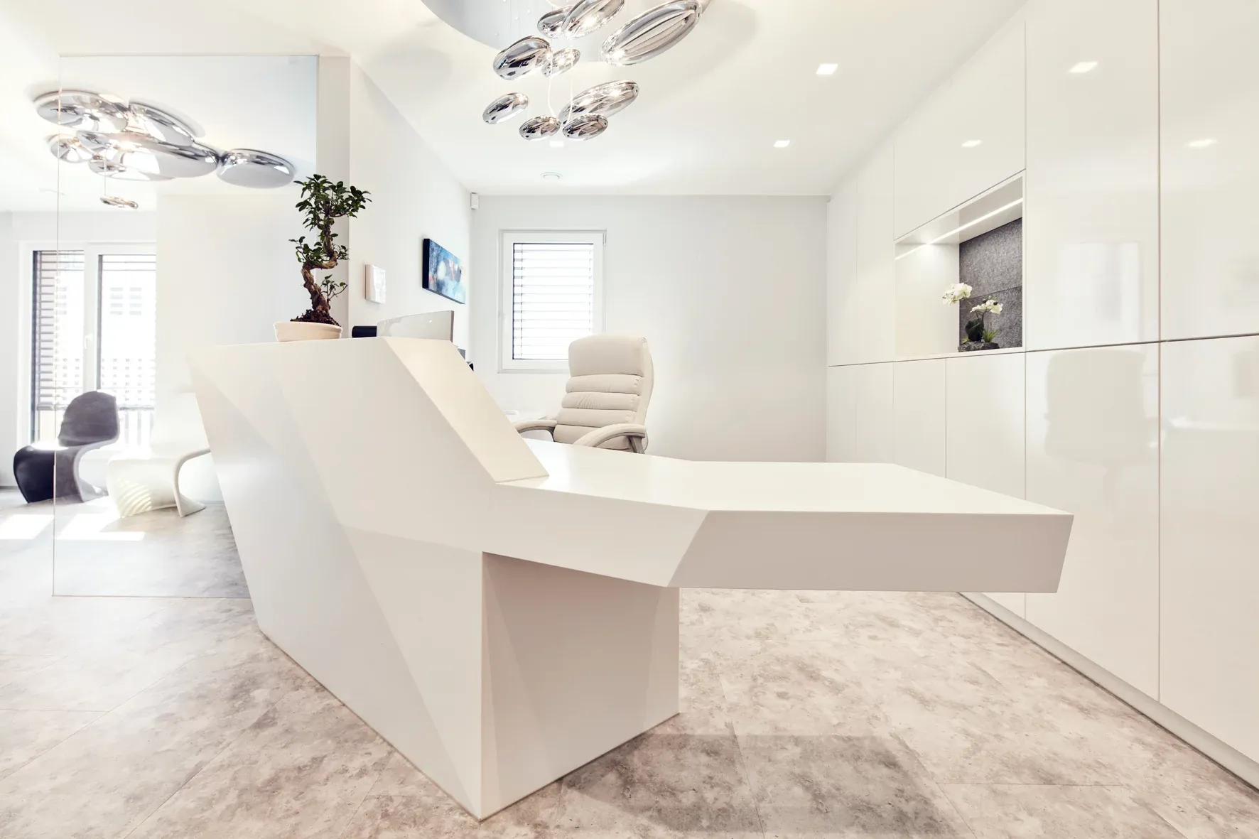 Empfangsbereich der Praxis mit moderner Theke in Weiß und modernen Deckenleuchten.