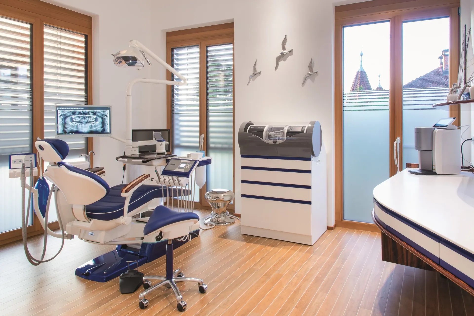 Behandlungszimmer in Segeloptik mit blauer Behandlungseinheit und Möwendekor an der Wand.